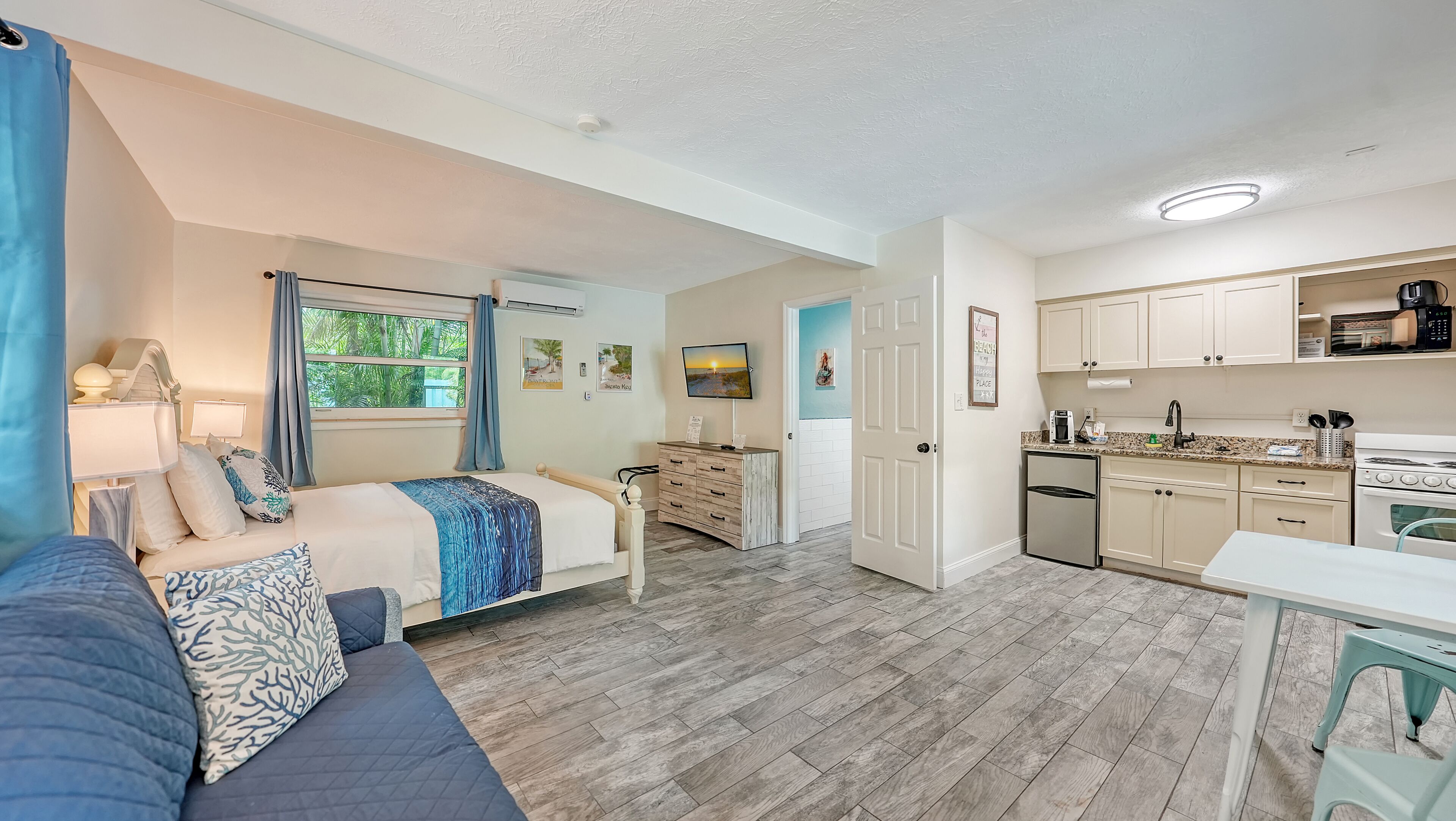 A compact living space with a bed, a sofa, a desk, a kitchenette, and a television.