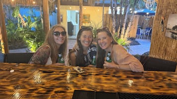 Eine Gruppe von Personen sitzt an einem Holztisch mit tropischem Dekor in einem Restaurant mit einem Reetdach und einem Außenbereich.