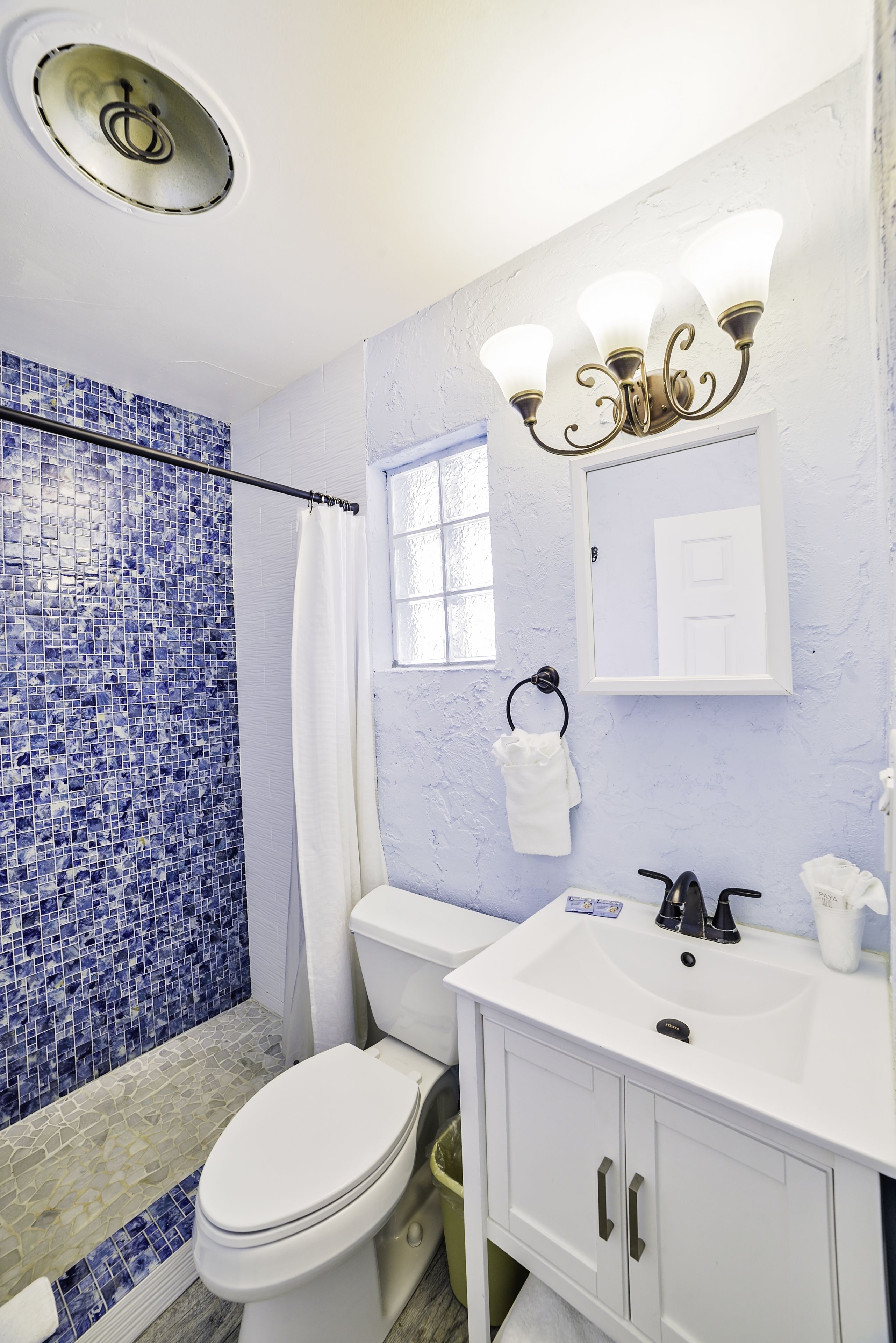 A bathroom with a white toilet, a sink with a mirror, and a shower with blue mosaic tiles.