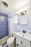 Um banheiro com vaso sanitário branco, pia com espelho e chuveiro com azulejos de mosaico azul.