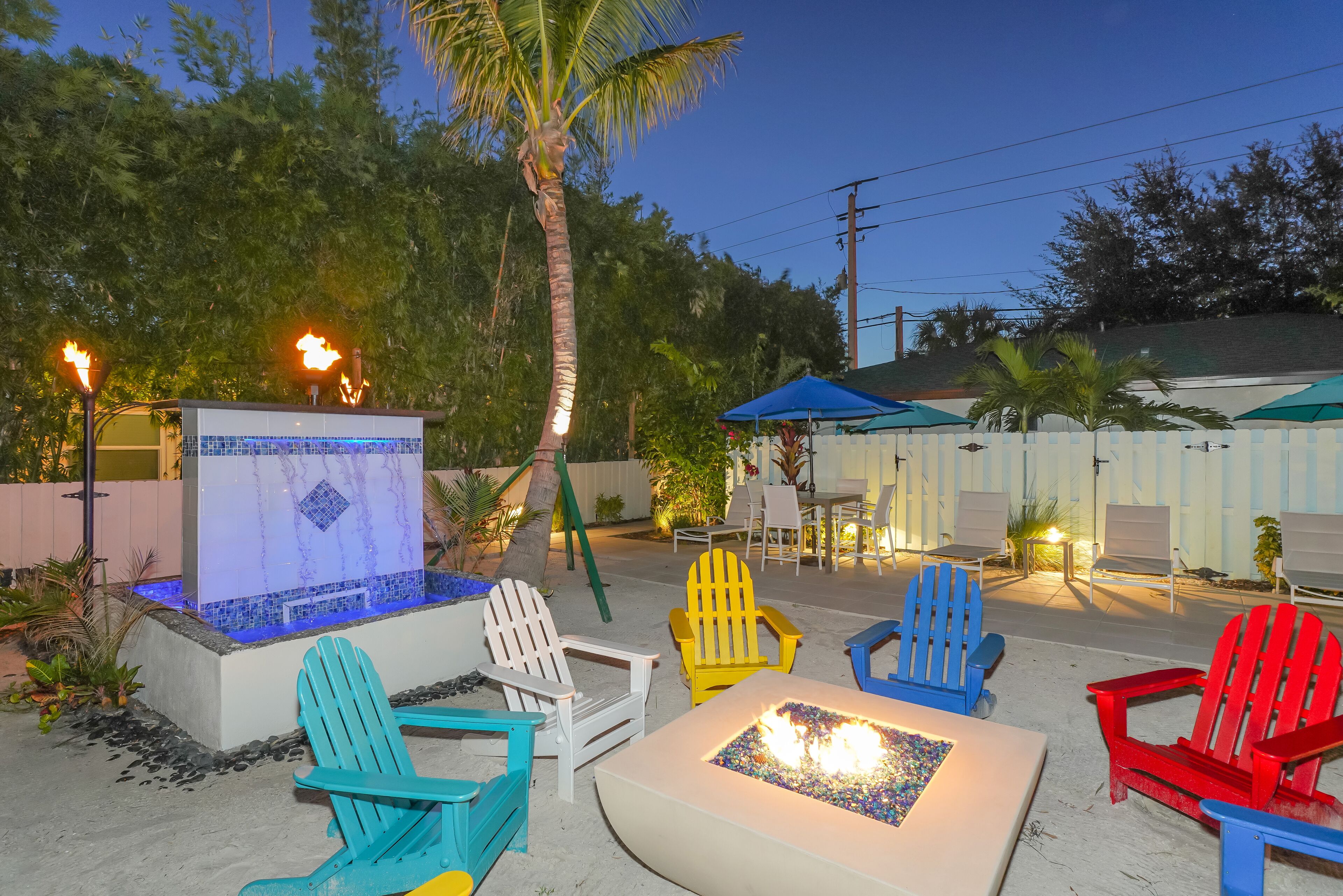 A patio area with colorful Adirondack chairs, a fire pit, and a hot tub.