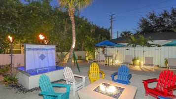 A patio area with colorful Adirondack chairs, a fire pit, and a hot tub.