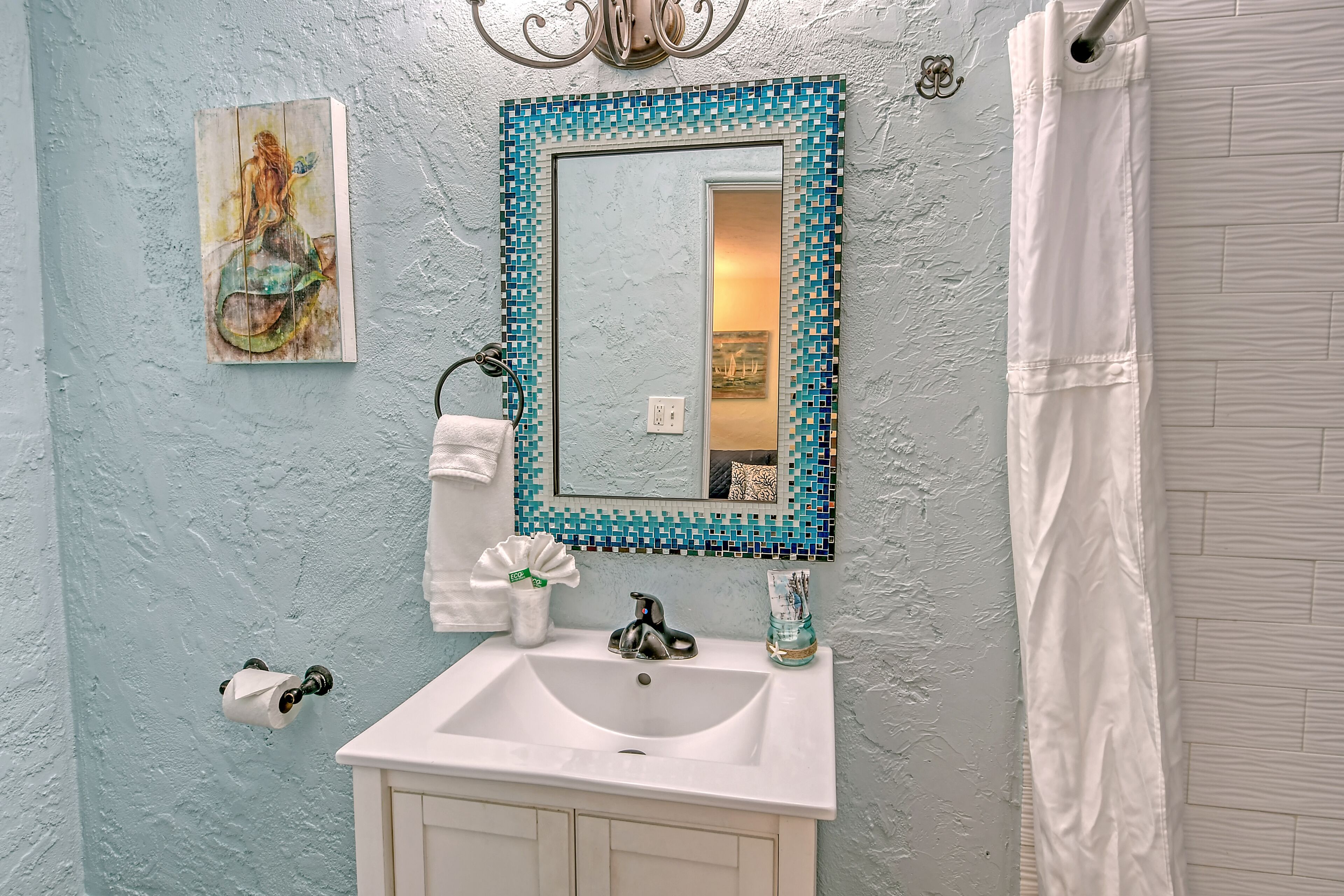 A bathroom with a white sink, a blue mosaic-framed mirror, a toilet paper holder, and a towel rack.