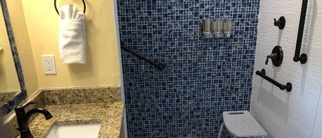 A bathroom with a granite countertop, a white sink, a shower with blue mosaic tiles, and a white toilet.