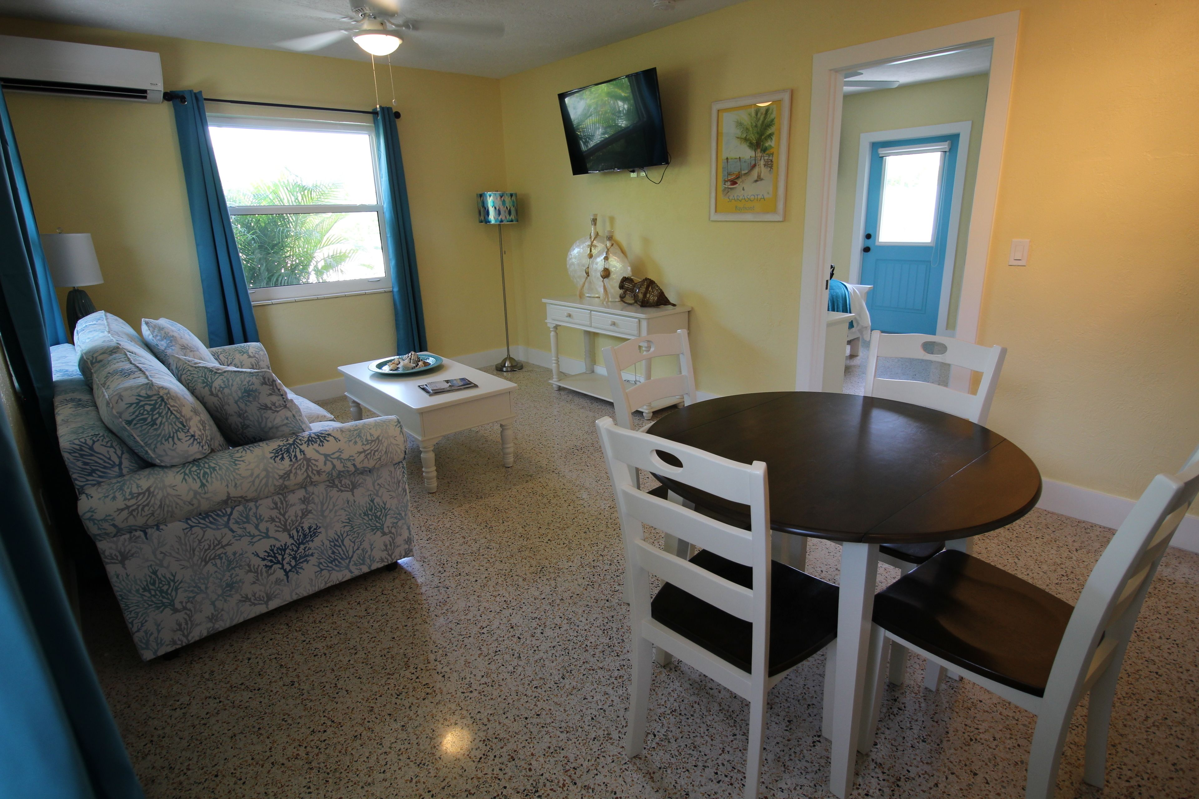 A living room with a sofa, coffee table, dining table with chairs, a TV, and a door with a window.