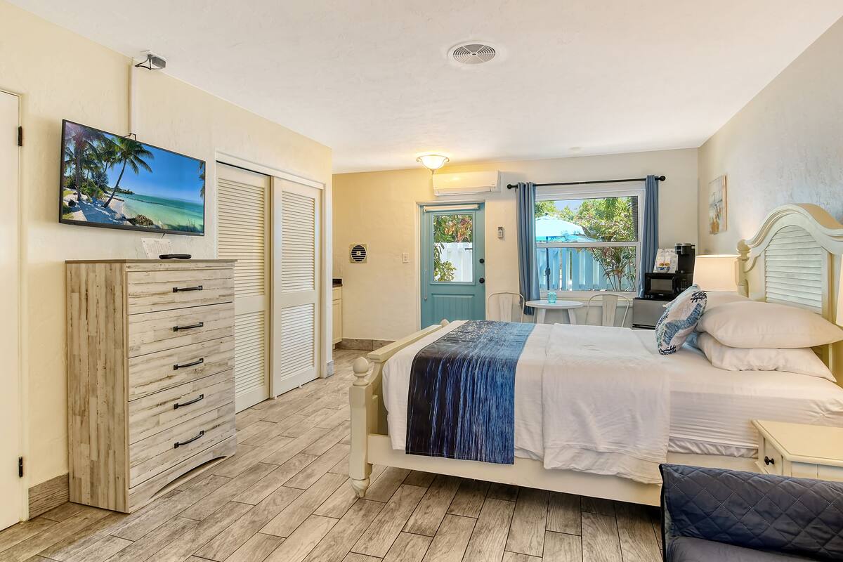 Un dormitorio con cama, cómoda, televisor y vistas al exterior.