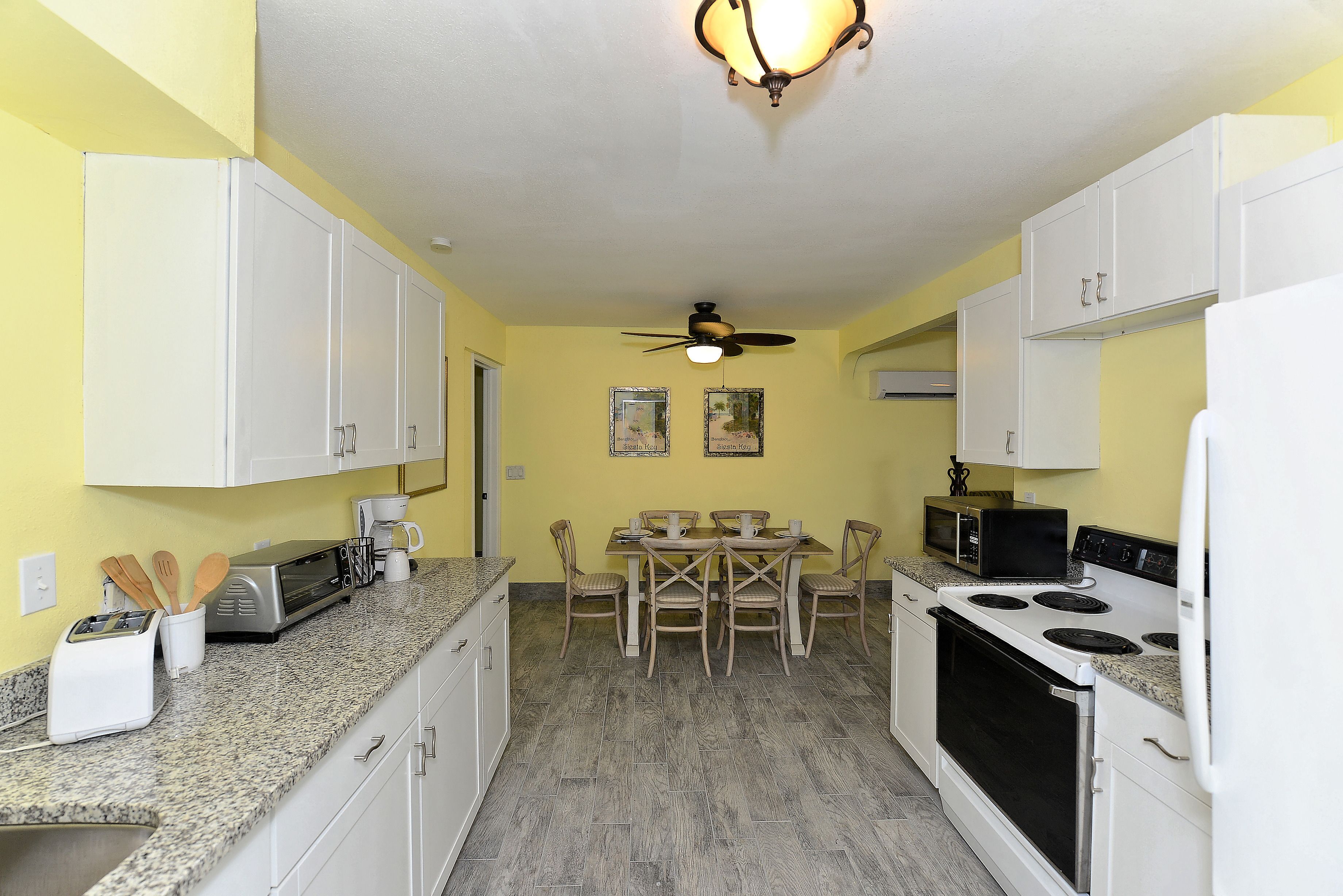 A compact kitchen with white cabinets, a microwave, a toaster, and a dining table with chairs.