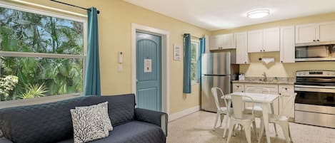 Un espacio habitable compacto con kitchenette, un sofá con cojín estampado, una mesa de comedor con sillas y vistas a zonas verdes.