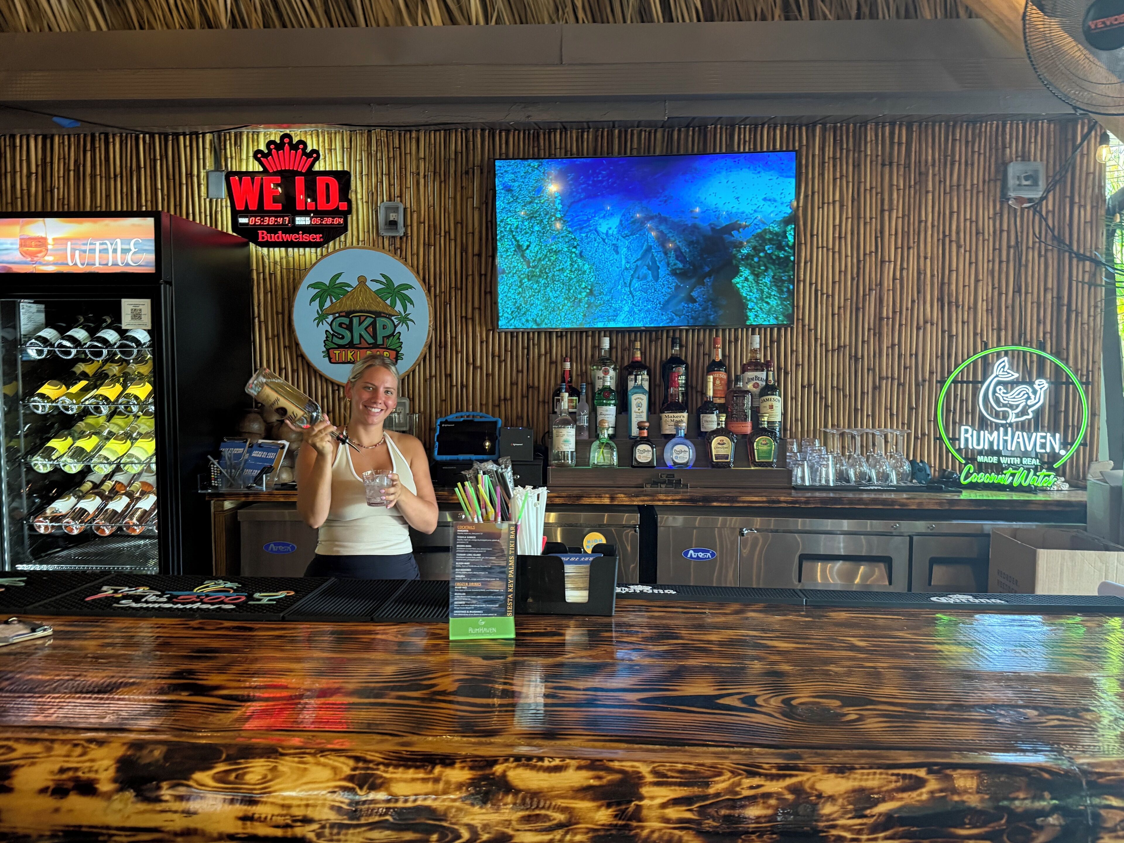 Een bar met een houten wand, een televisiescherm en verschillende drankflessen.