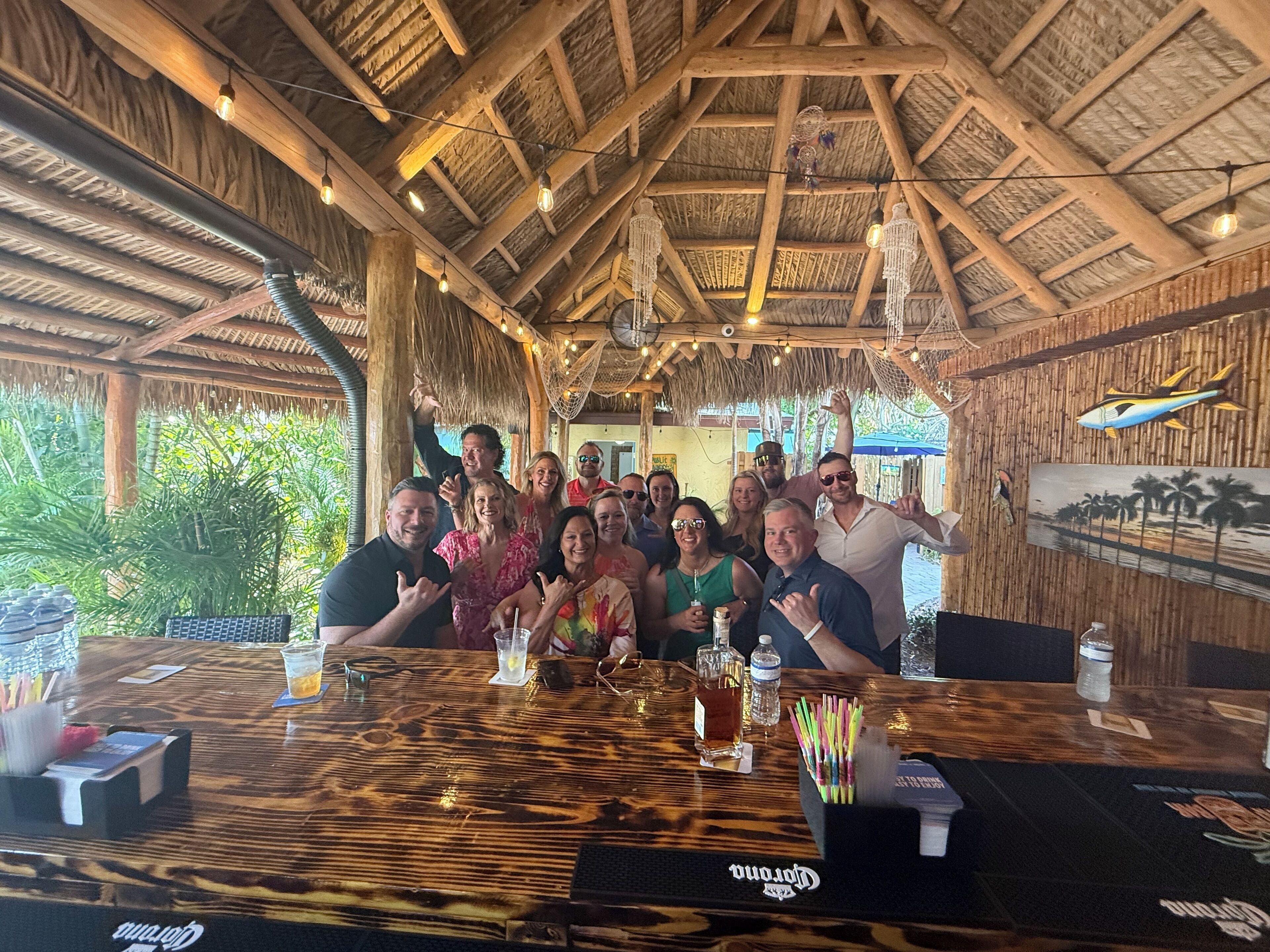 A group of people seated at a wooden table inside a rustic building with a thatched roof and wooden beams.