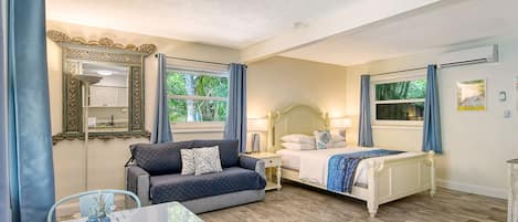 A hotel room with a bed, a sofa, a table, and a mirror.