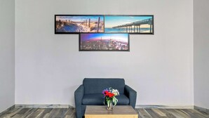 Un salon avec un canapé gris, une table basse en bois et un vase de fleurs. Trois tableaux encadrés sont accrochés au mur.