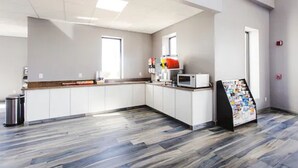 Une cuisine moderne avec des meubles blancs, un four à micro-ondes et une machine à café. On y trouve également un porte-revues et une poubelle.