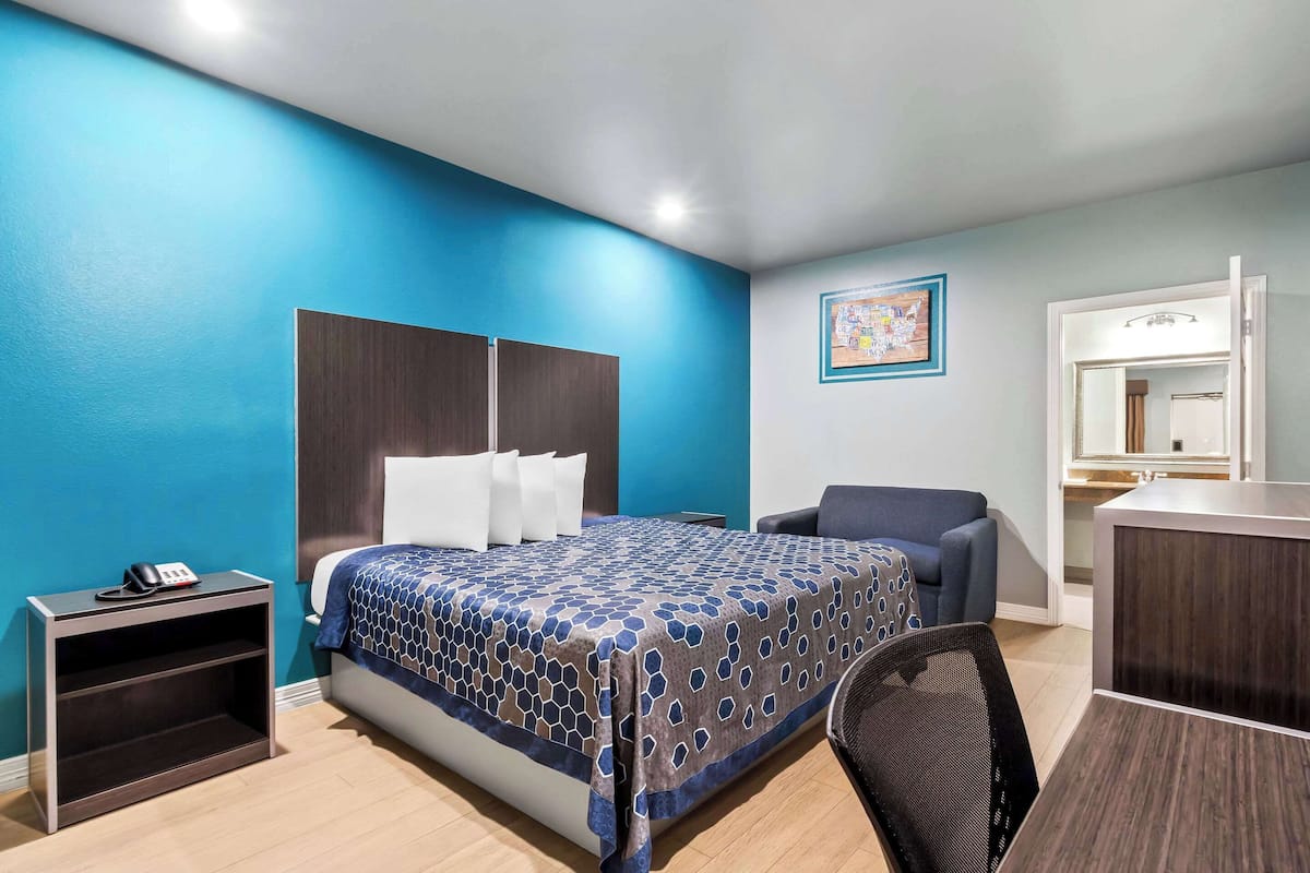 A hotel room with a bed, a desk, a chair, a nightstand, and a mirror.