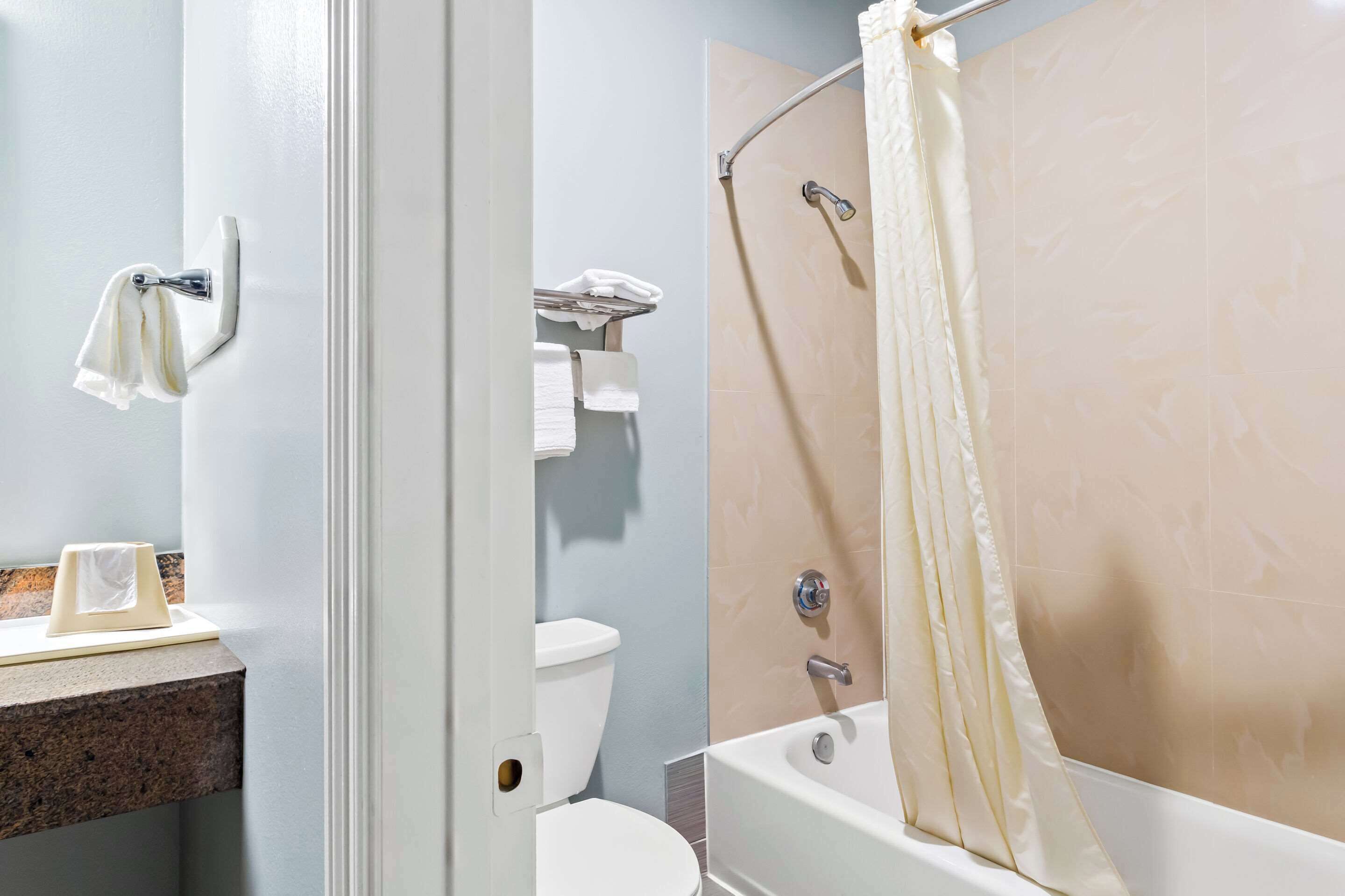 A bathroom with a toilet, a sink with a towel holder, and a bathtub with a shower curtain.