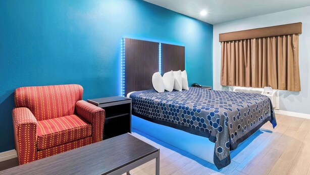 Une chambre d’hôtel avec un mur bleu, un lit recouvert d’une couvre-lit à motifs, un fauteuil rouge, une petite table et une table de chevet.