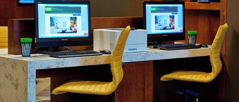 A modern office space with two computer workstations, each with a monitor, keyboard, and mouse. There are two yellow chairs with black mesh footrests. A printer is visible on the counter.