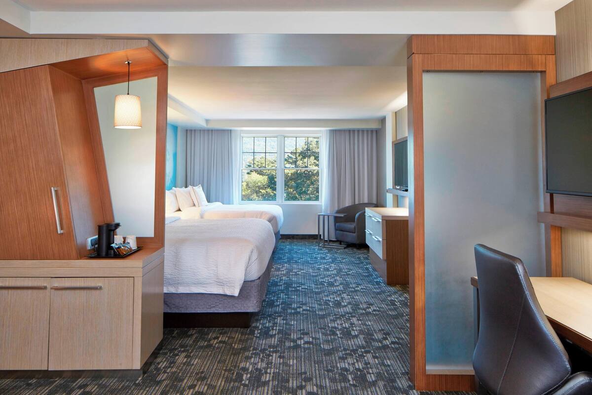 A hotel room with a bed, a desk, a chair, a TV, and a large window.
