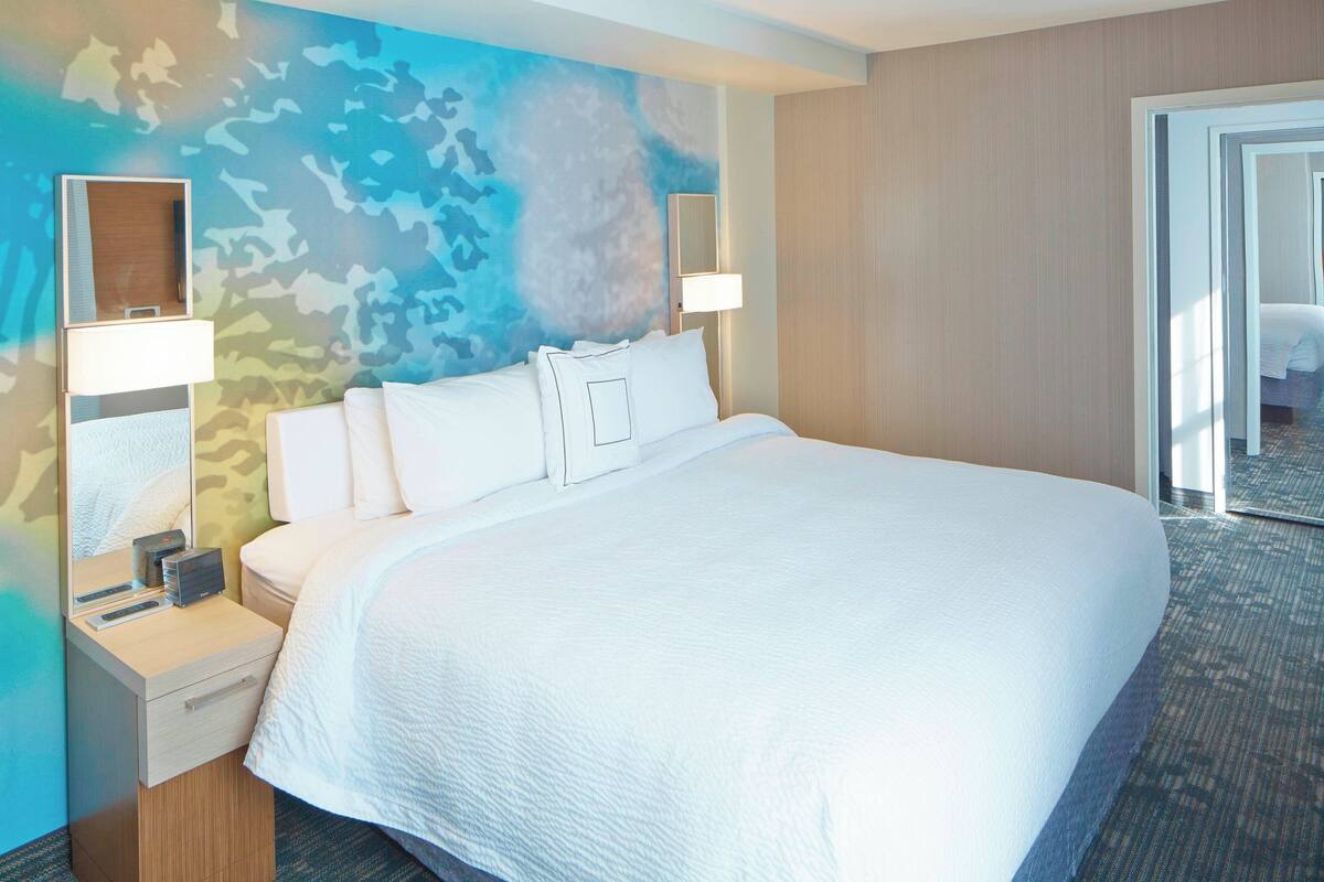 A hotel room with a large bed, two bedside tables, a nightstand, a mirror, and a wall with a camouflage pattern.