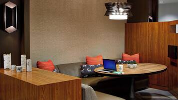 A modern hotel room with a wooden reception desk, a round dining table, a laptop, and a television.