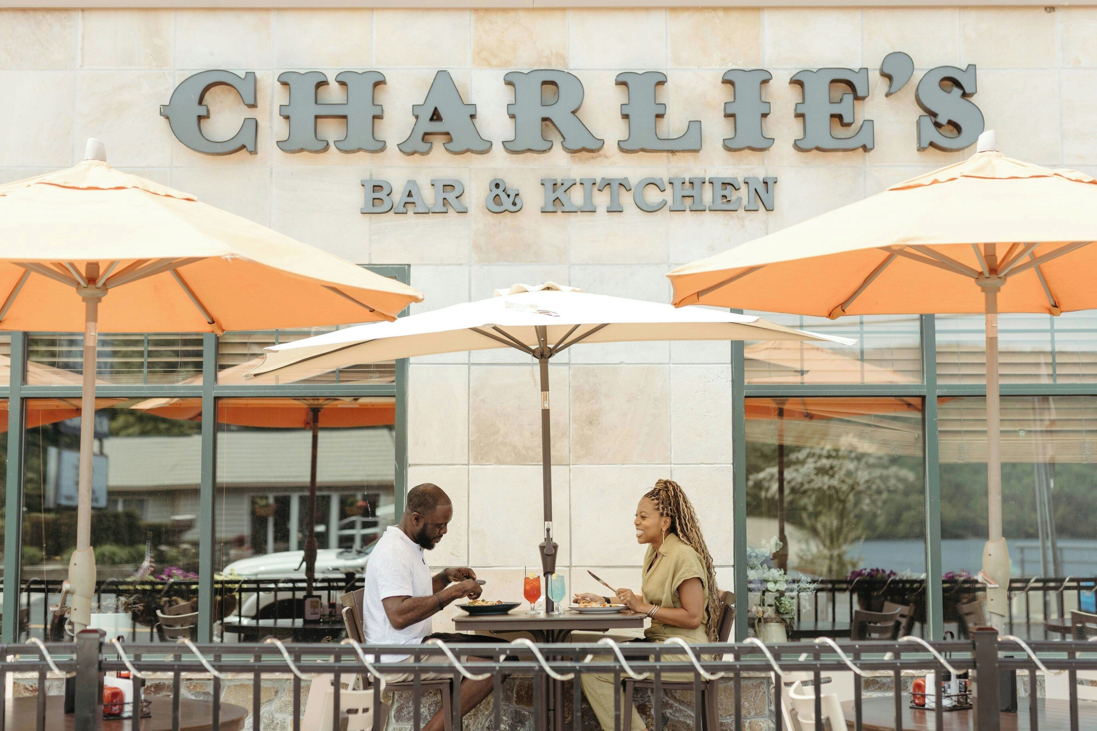 An outdoor dining area at Charlie's Bar & Kitchen with large umbrellas and a view of the water.