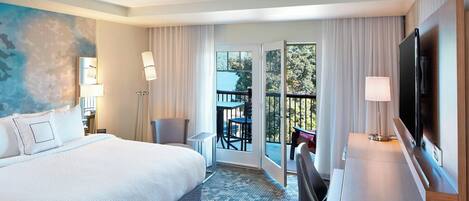 A hotel room with a large bed, a desk with a TV, a balcony with a table and chairs, and a painting on the wall.