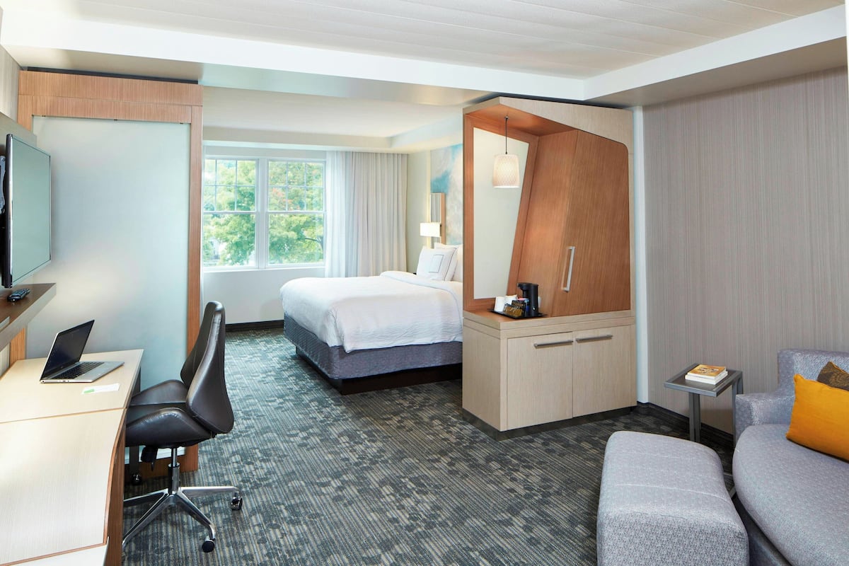 A hotel room with a bed, a desk with a laptop, a chair, a small table, and a sofa.