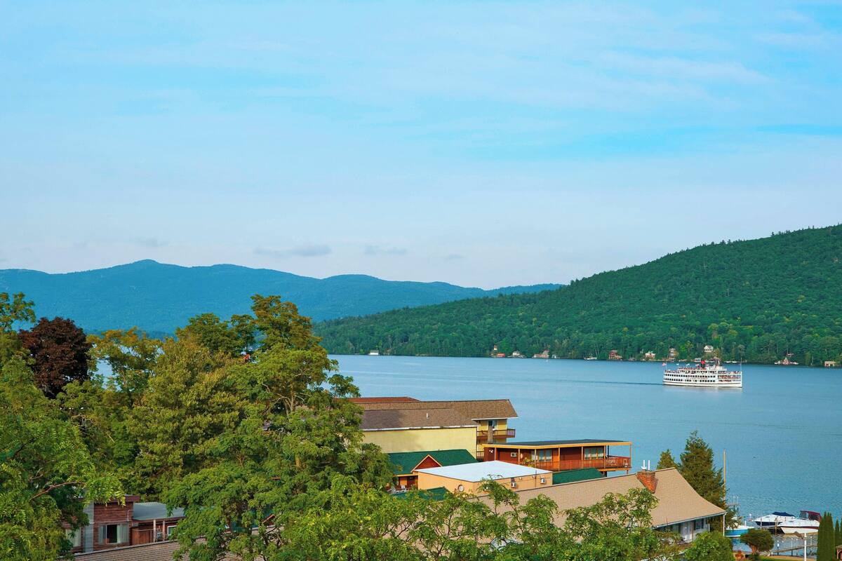 A lakeside view with a boat, buildings, and hills.