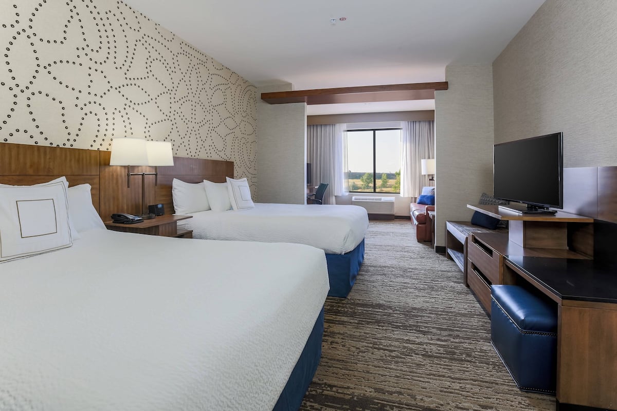 A hotel room with two beds, a desk, a TV, and a large window with a view.