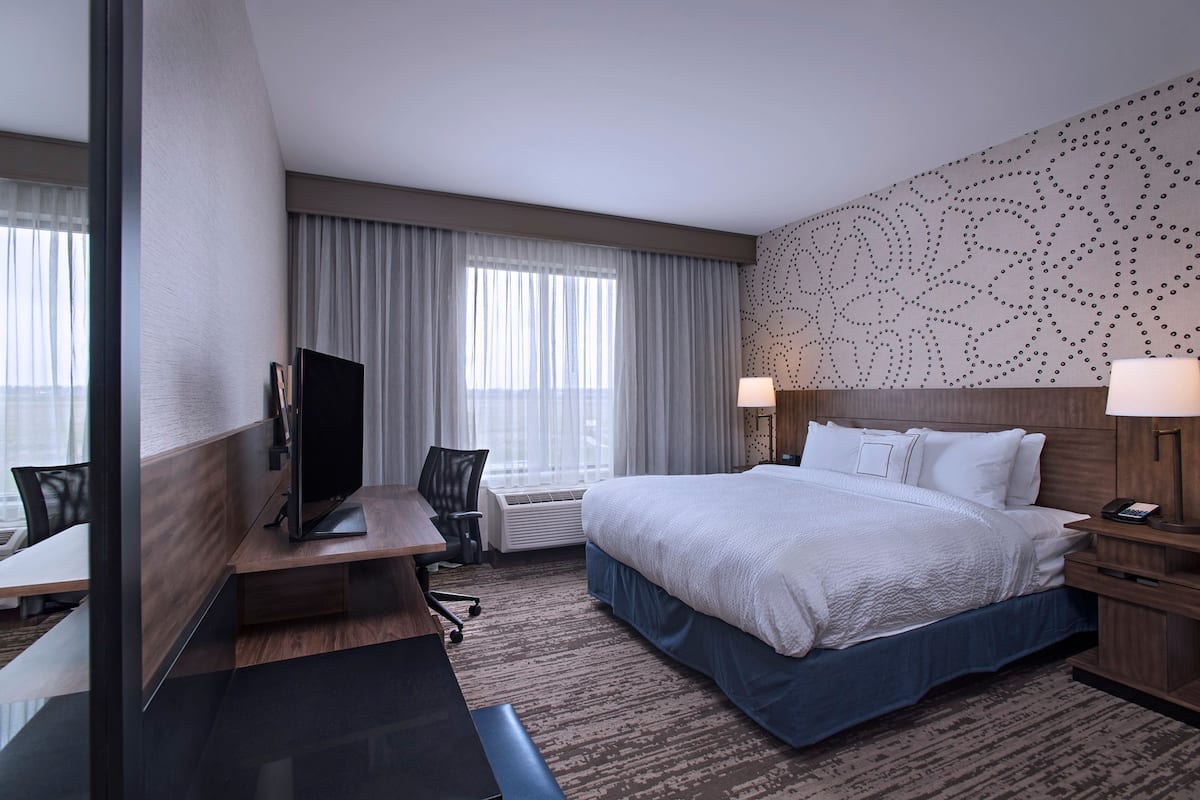 A hotel room with a bed, desk, TV, and a patterned wall.