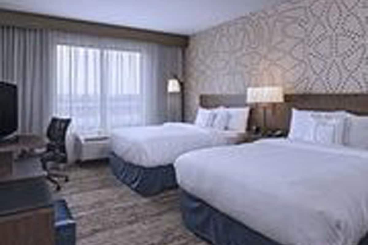 A hotel room with two beds, a desk, a chair, and a television.