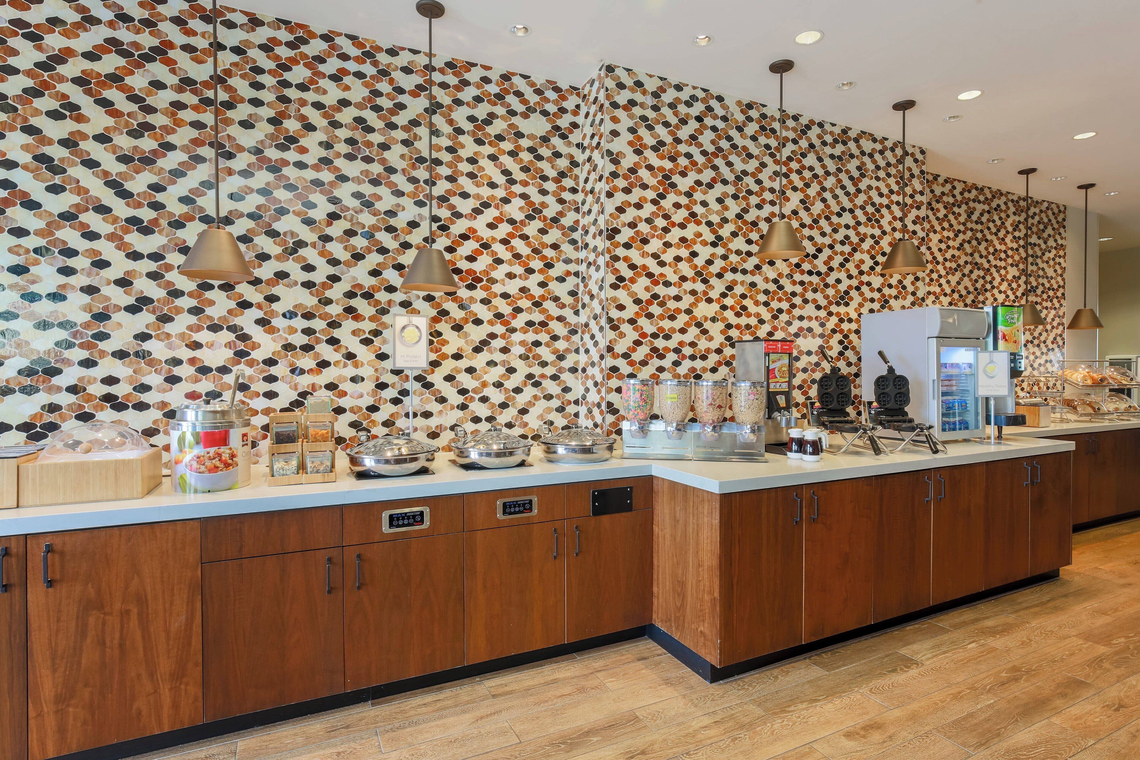 A modern kitchen with a patterned backsplash, a central island with a refrigerator, and overhead pendant lighting.