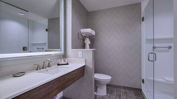 A modern bathroom with a large mirror, dual sinks, a toilet, and a shower area.