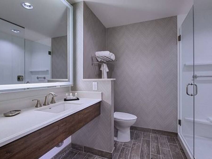 A modern bathroom with a large mirror, dual sinks, a toilet, and a shower area.