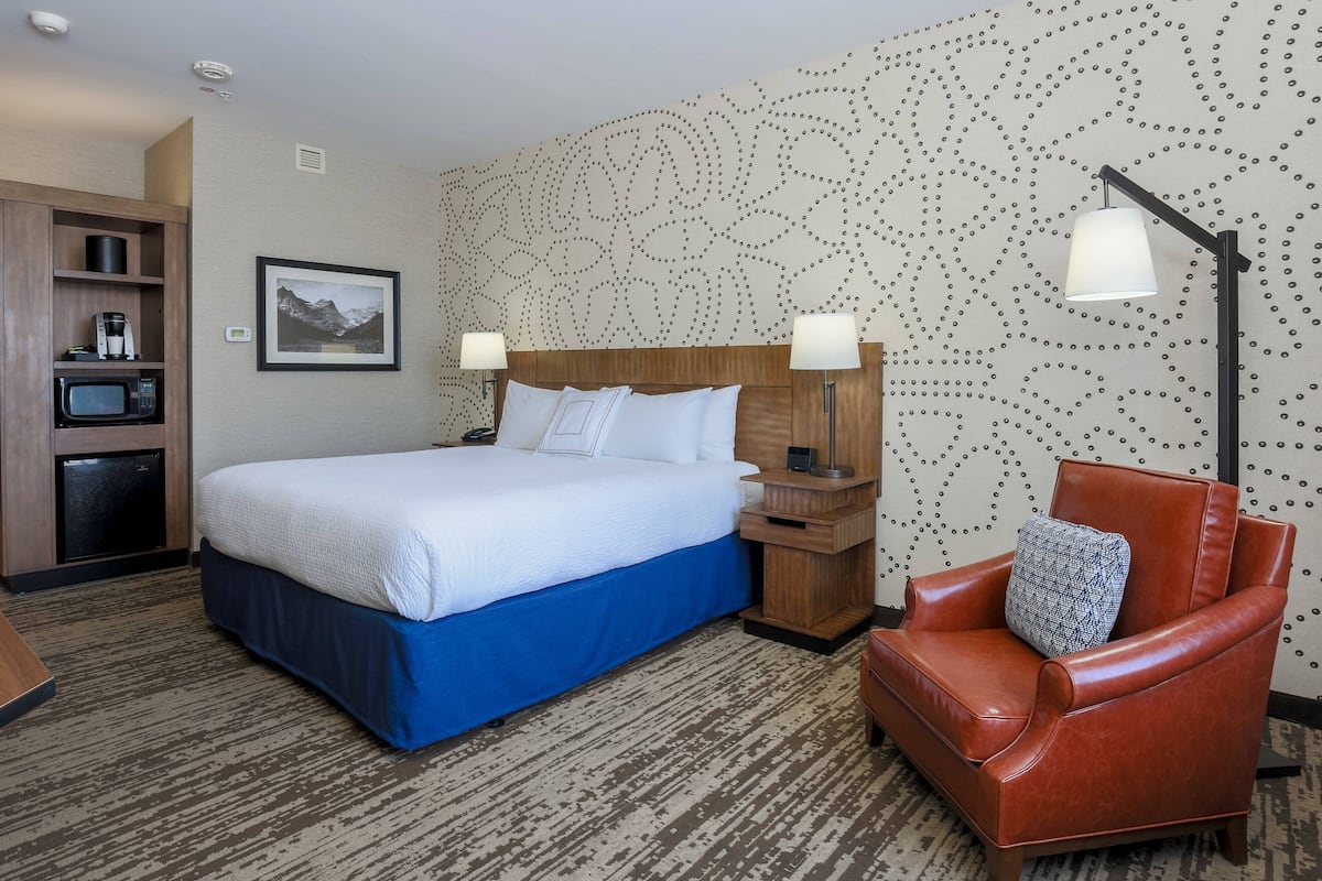 A hotel room with a large bed, a wooden nightstand, a red leather chair, and a patterned wall.