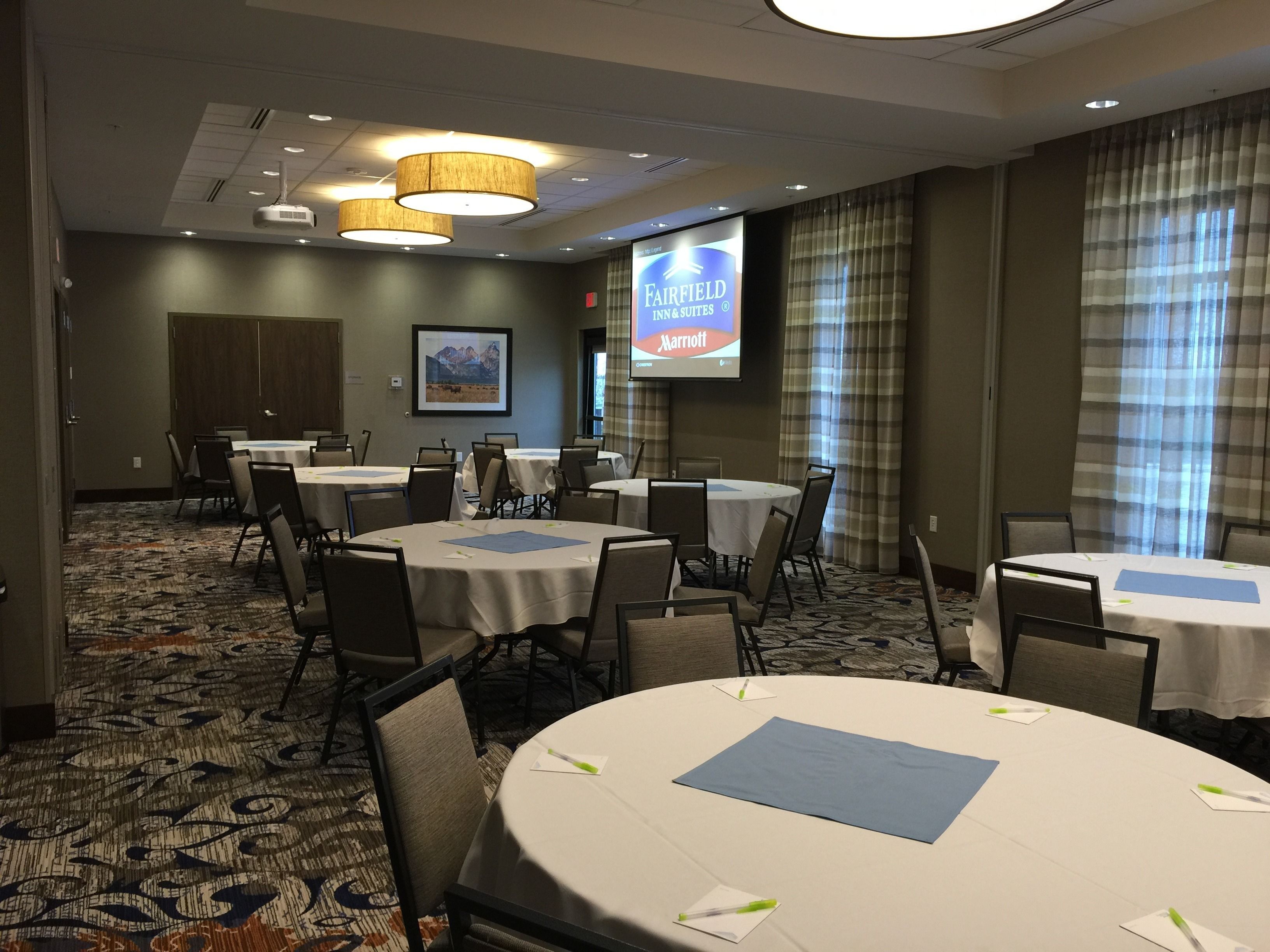 A conference room with round tables, chairs, and a large screen displaying the Fairfield Inn & Suites logo.