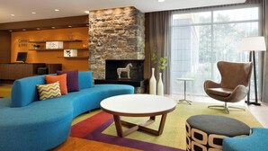 A modern living room with a stone fireplace, a blue sofa, a round coffee table, and a brown armchair. - Fairfield Inn & Suites Lancaster East at The Outlets (Lancaster)