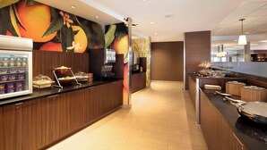 A hotel reception area with a fruit-themed mural, a self-service beverage station, and a buffet counter. - Fairfield Inn & Suites Lancaster East at The Outlets (Lancaster)