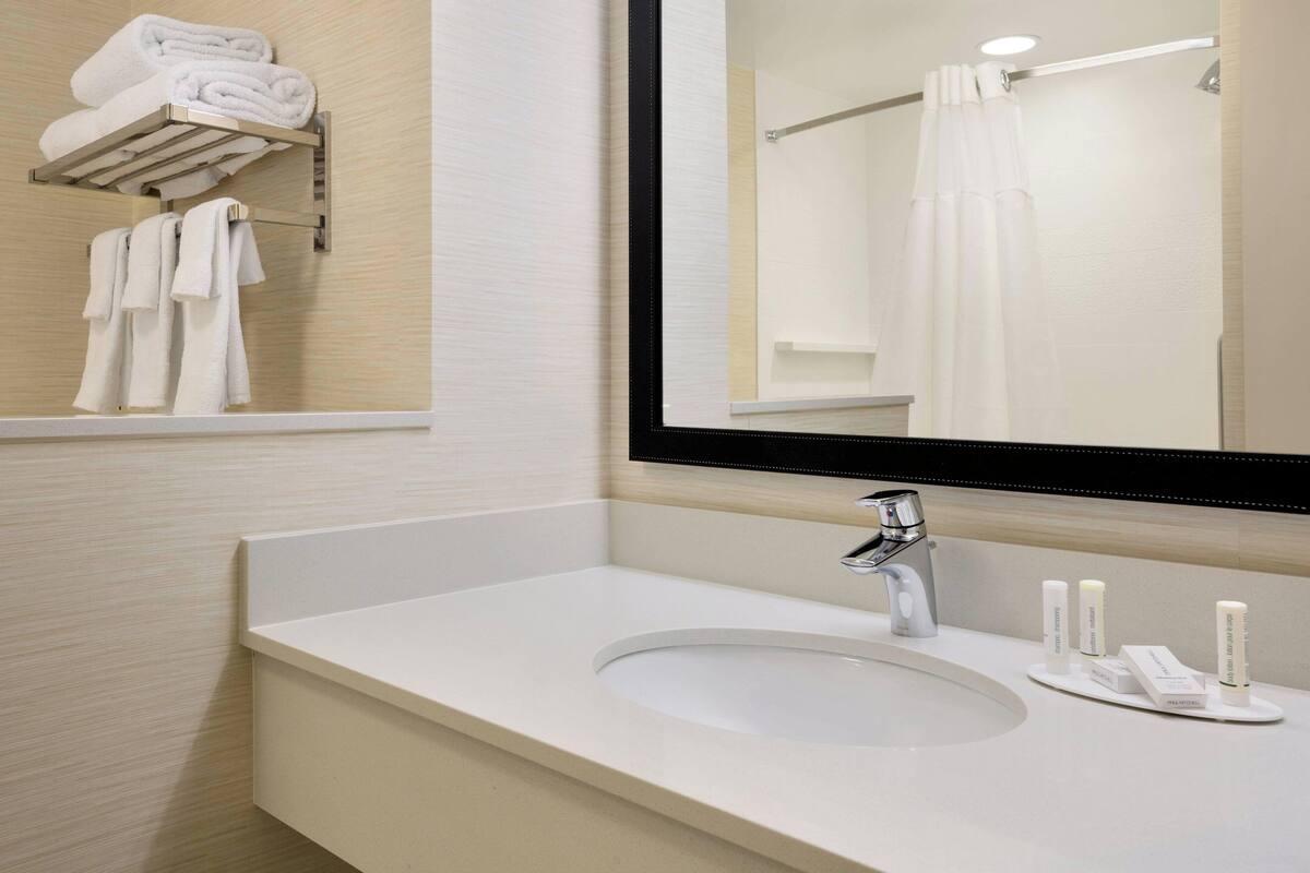A modern bathroom with a white sink, a mirror, and a towel rack with folded towels.