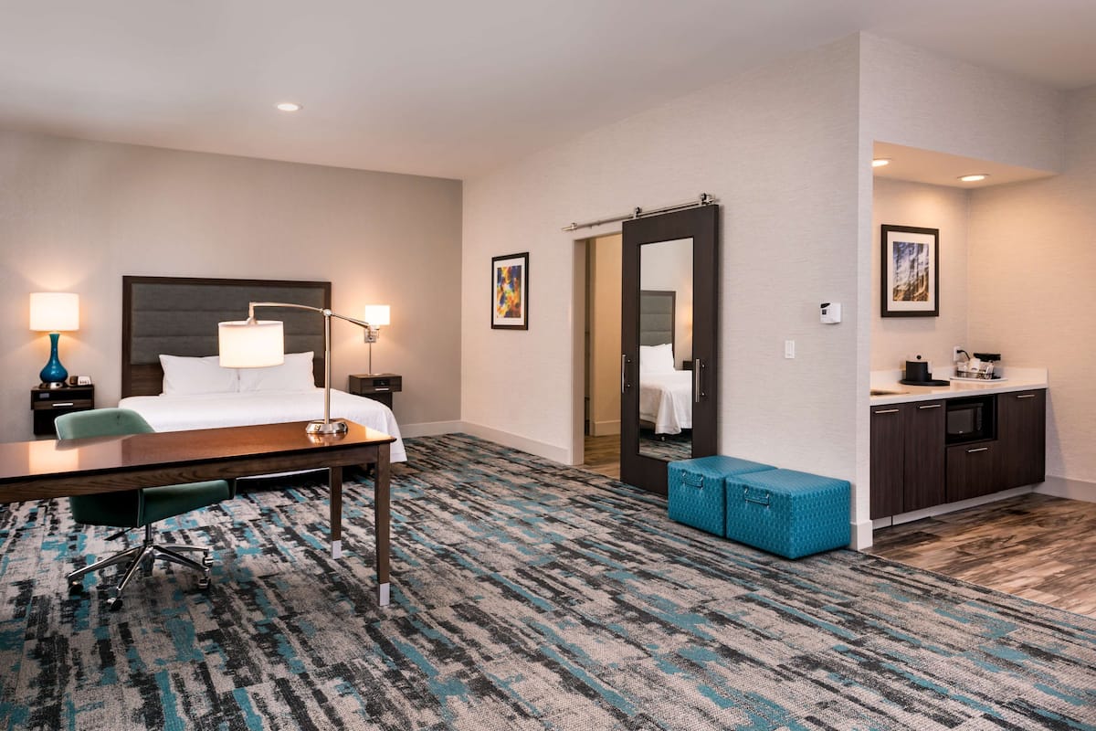 Ein Hotelzimmer mit Bett, Schreibtisch, Stuhl und einer Küchenzeile.