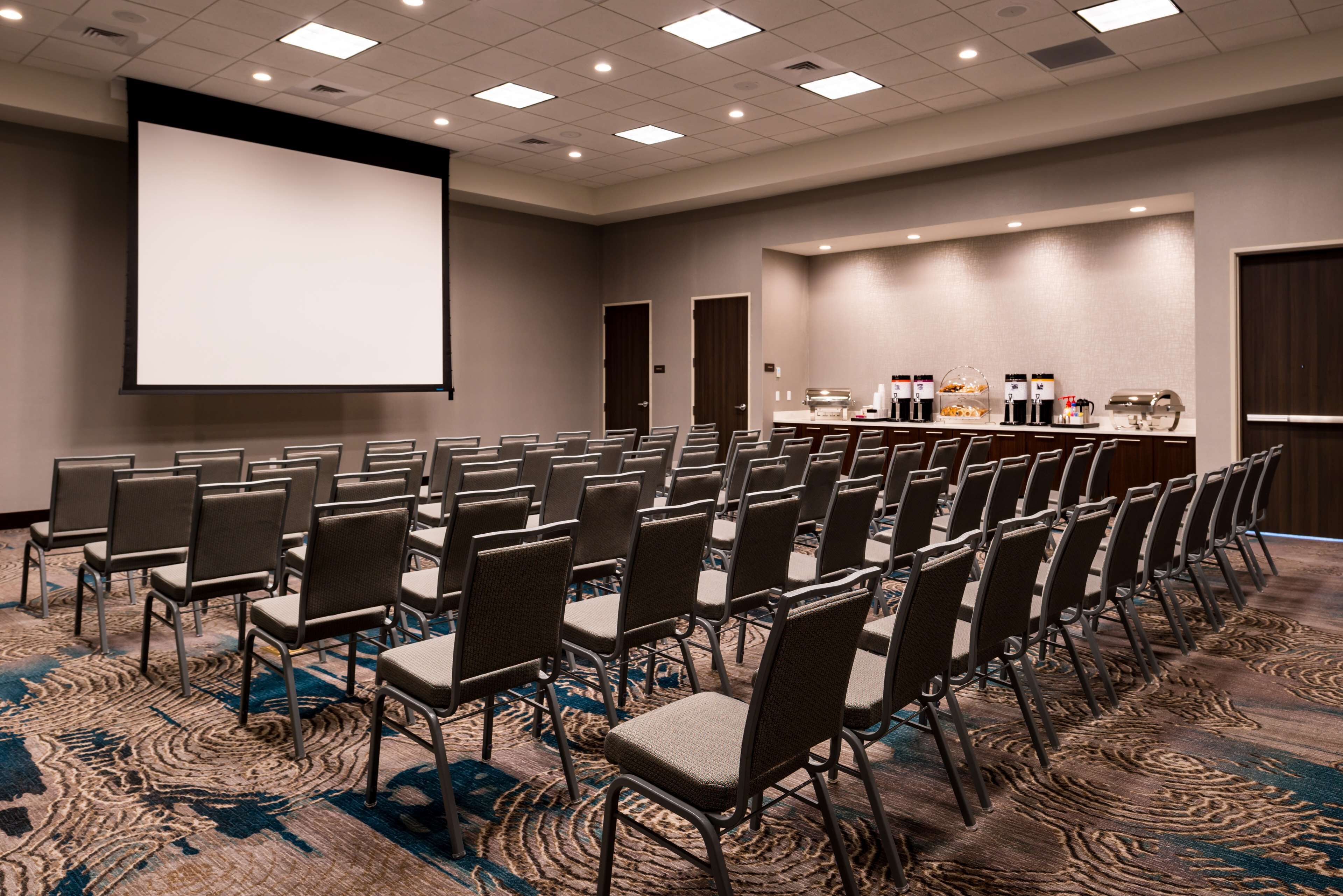 A conference room with rows of chairs, a large screen, and a buffet area with coffee and snacks.