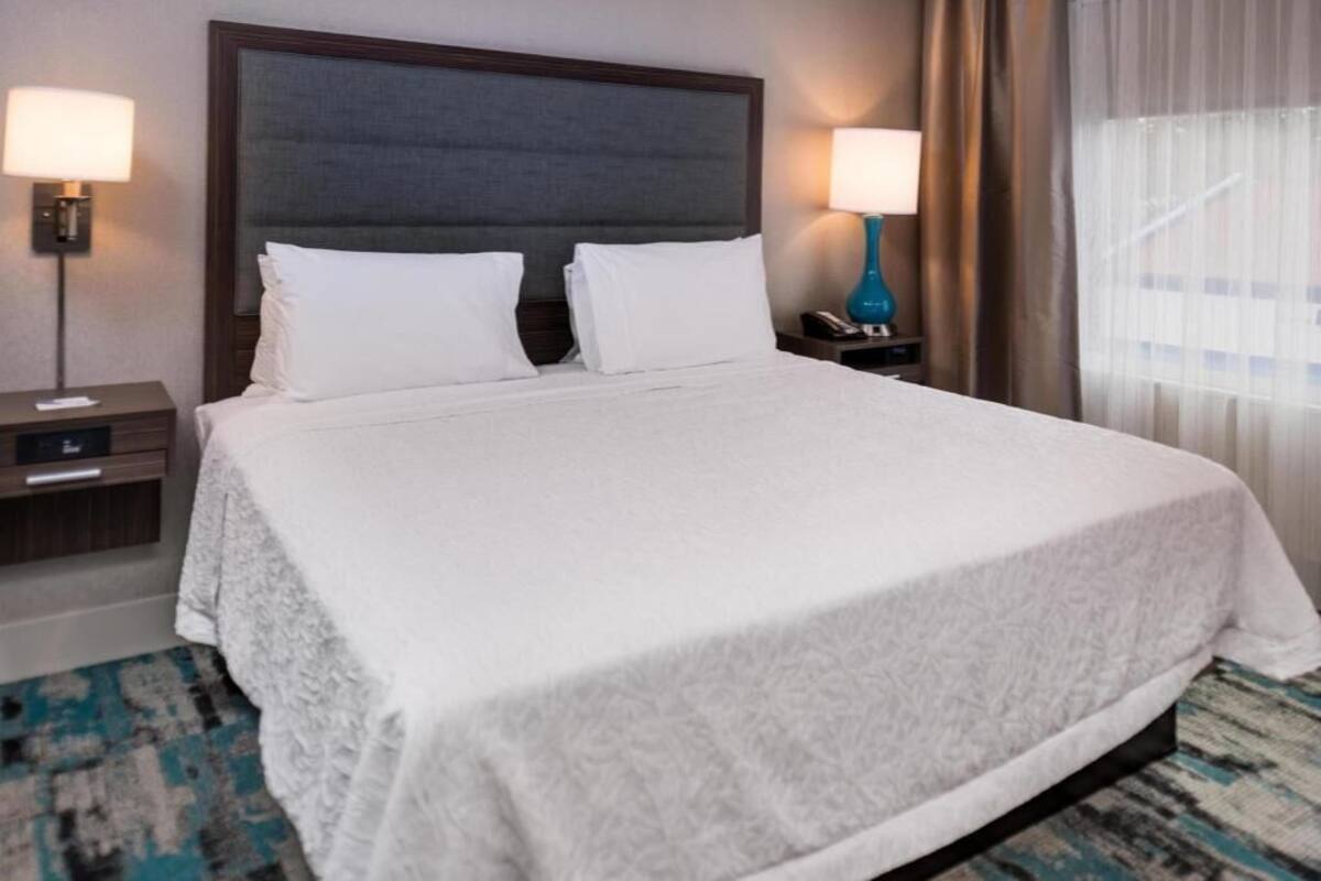 Ein Hotelzimmer mit einem großen Bett, zwei Nachttischen, einem Fenster mit Vorhängen.