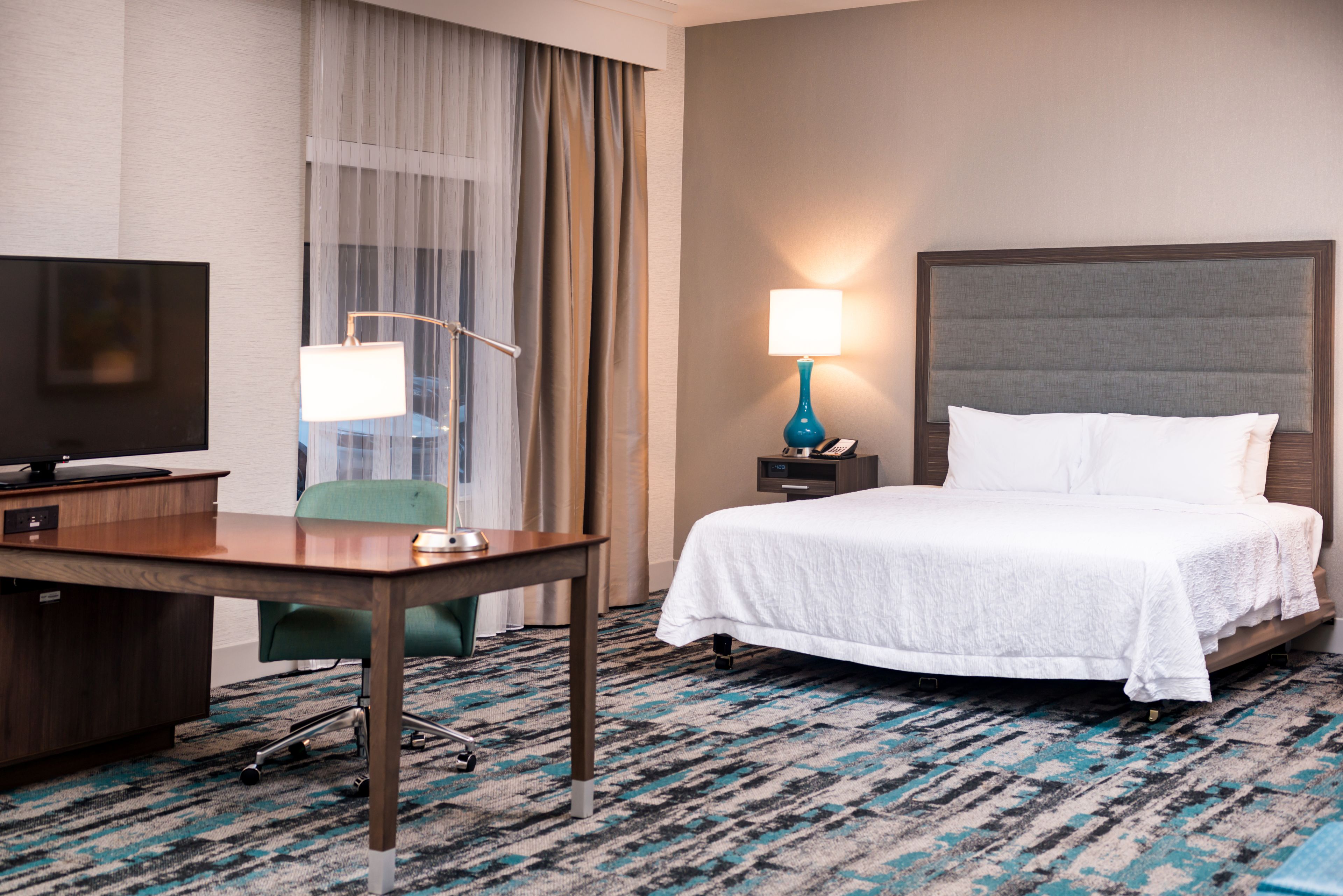 A hotel room with a bed, a desk with a computer, a lamp, and a TV.