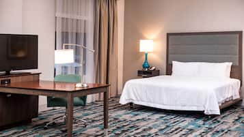 A hotel room with a bed, a desk with a computer, a lamp, and a TV.