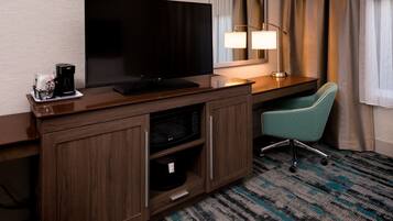 A hotel room with a flat-screen TV, a coffee maker, a lamp, a desk, and a teal chair.