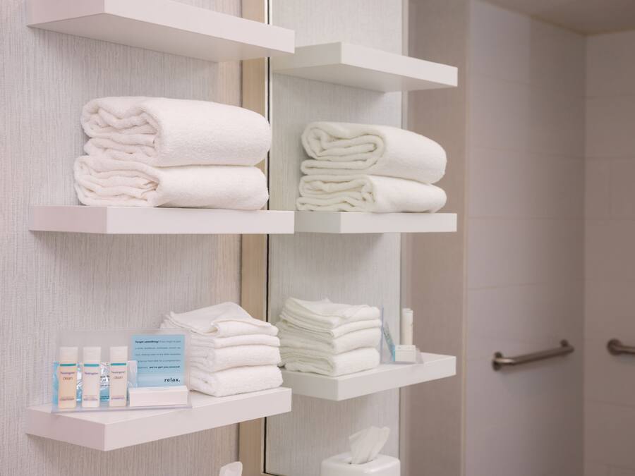 Casa de banho com toalhas brancas, produtos de higiene e um espelho.