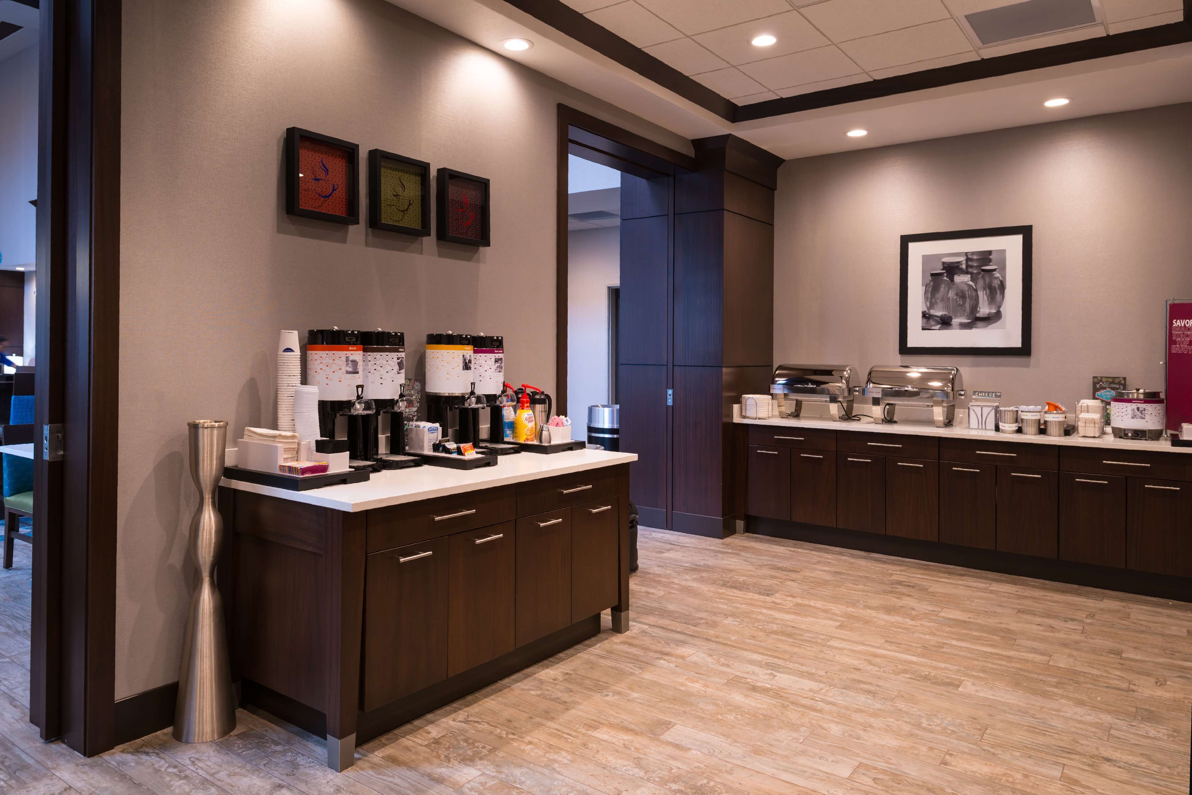 A modern kitchen with a central island, equipped with coffee machines, a refrigerator, and various kitchen appliances.