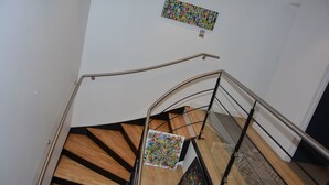 A staircase with wooden steps and metal railings, leading to a landing with a colorful abstract painting. - Le Matisse (Pau)