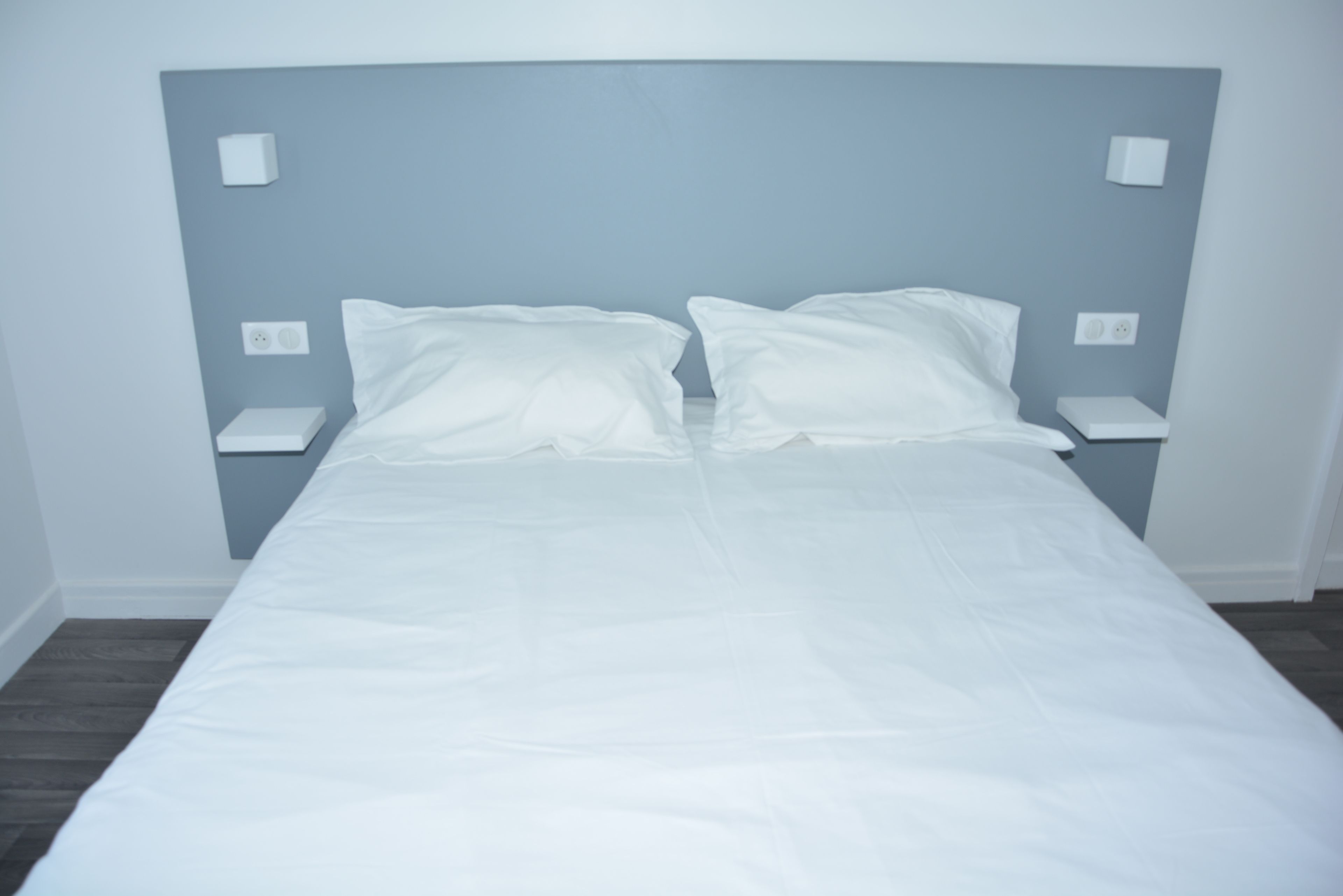 Un llit ben fet amb llenços blancs a una habitació amb un panell del capçal blau cel i nits abans.