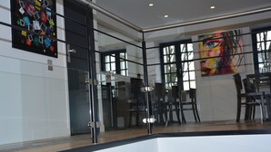 A modern interior with a glass partition, a dining area with chairs, and a colorful painting on the wall. - Le Matisse (Pau)